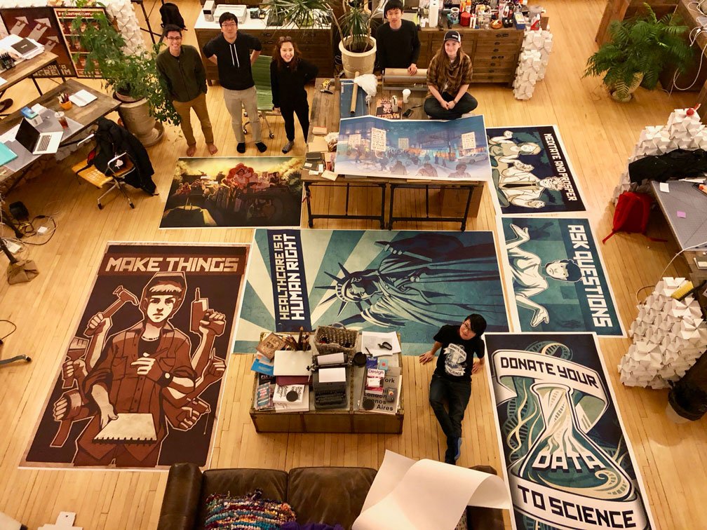 Overhead shot of Invo artwork printed very large, spread out on the floor with the studio team scattered around smiling